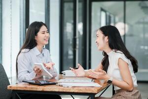 Two women in a modern office setting, discussing work with digital devices and documents on the table. photo