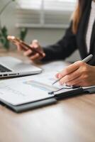 Professional woman reviewing charts and graphs at a desk, using a tablet and smartphone for business analysis. photo