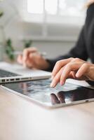 Close-up of hands using a tablet and laptop in a bright office environment, symbolizing digital work and technology. photo