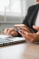 Close-up of a person using a smartphone and laptop in a bright office, showcasing modern technology and business communication. photo