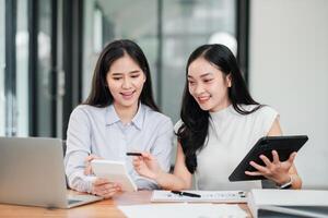 Two women working together in a contemporary office setting, using digital devices and discussing documents. photo