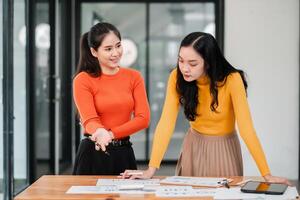 Two Young Women Collaborating on a Project in a Modern Office Setting with Documents and Digital Devices photo
