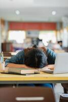 Exhausted Student Asleep on Desk with Laptop and Books in a Classroom Setting photo