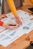 Collaborative Teamwork Analyzing Business Reports with Graphs and Charts on Wooden Desk in Modern Office Setting photo