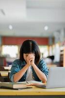 Student Deep in Thought at Library Desk with Open Books and Laptop in Bright Study Environment photo