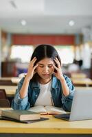 Young Woman Studying in Library with Laptop and Books, Feeling Stressed and Overwhelmed by Academic Workload photo