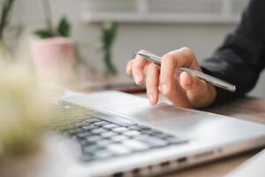 Close-up of Hand Using Pen on Laptop Touchpad in Modern Office Setting with Greenery in Background photo
