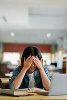 Stressed Student Studying in Library with Laptop and Books, Overwhelmed by Academic Pressure and Deadlines photo