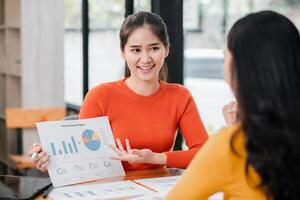 Two women engaged in a business meeting, reviewing marketing reports and data analysis in a contemporary office environment. photo