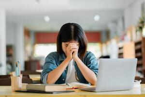 A student in a library feeling stressed while studying with a laptop and books, symbolizing academic pressure and the pursuit of knowledge. photo