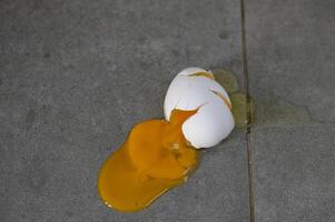 Eggshell cracks open on a cold, gray surface revealing bright golden yolk in daylight photo