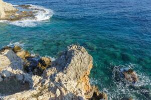 Serene coastal view captures the gentle waves lapping against rocky cliffs under a clear blue sky. photo
