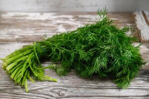 Freshly harvested dill resting on a rustic wooden surface with textured patterns in natural light photo