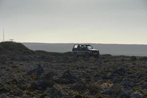 A lone vehicle navigates the rocky terrain under the expansive, cloudy sky at dusk. photo
