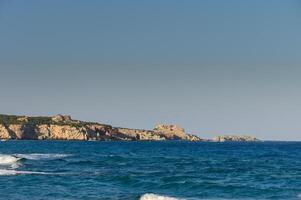 Waves crashing gently on a tranquil shore with rocky cliffs under a clear sky. photo