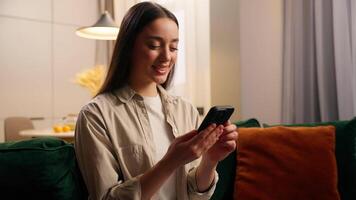 Caucasian woman female lady girl at home relaxing at couch holding mobile phone smiling browsing social media app showing green screen smartphone display mock up chroma key cellphone website internet video