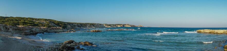 Serenity at the shoreline tranquil waves caress a sunlit rocky beach on a beautiful afternoon. photo
