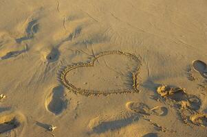 A heart drawn in soft sand on a sunlit beach, capturing lo photo