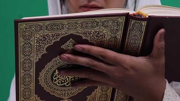 A person is holding a Quran and reading it, showing the decorative details on the cover, and focusing on the hands and book, isolated on a green background or green screen video