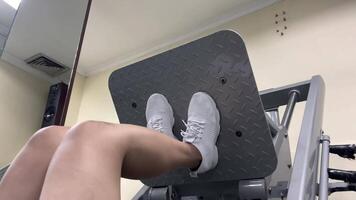 A person is using a leg press machine for exercise. They are wearing white shoes and a patterned skirt. They are in a gym setting with tan walls. video