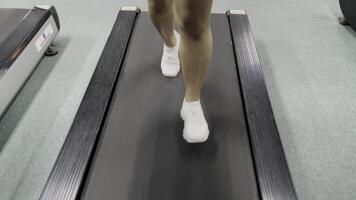 A close up view of white athletic shoes and legs on a treadmill. The treadmill belt is gray with a black outline. The flooring is a light gray color. video