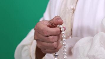 A person holds a string of pearl beads in their hand, the beads are smooth and shiny, perfect for prayer or meditation. isolated on a green background or green screen video