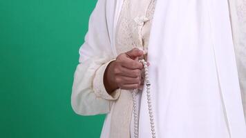 A person wearing a white garment holds a string of pearl beads in their hand, the person's arm is visible along with the clothes they are wearing, isolated on a green background or green screen. video