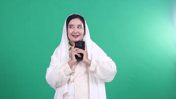 A person wearing a white veil looks at a mobile phone while holding it in their hands, isolated on a green background or green screen video