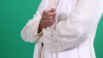 Close-up of hands holding a string of pearl-like beads, person wearing white clothing, the image shows only the arms and hand, isolated on a green background or green screen video