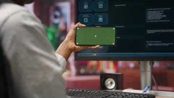 Woman using green screen smartphone to learn how to use AI LLM chatbot on computer screen in home office. Person watches tutorial on mockup phone about artificial intelligence chatbots, camera B video