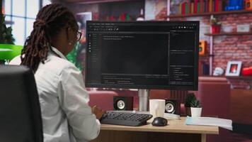 IT technician in home office looking at UI on computer monitor, executing programming script. Remote employee using coding application to write and test code in modern apartment, camera B video