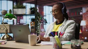 Teleworker listening music while typing on notebook keyboard in home office, writing emails. Remote employee wearing headphones using laptop, finishing project tasks, camera A video