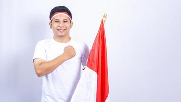 Handsome Indonesian Young Man Raising Fist in front of His Chest while Holding Country Flag photo
