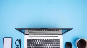 Top View of Working Space with Laptop, Mouse, Coffee Cup, Smartphone, and Glasses on Blue Background photo