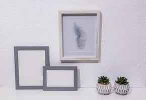 Stylish minimalist decor in light colors on a white table in a modern space. Two gray photo frames, a painting, pots. Front view. eco items.