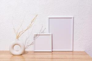 Home decor elements in a light style with white photo frames, a vase made of natural material with dry tree branches on wooden countertop. Front view