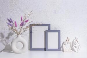 decorative objects on a white table in the interior of a modern space. A photo frame, lilac dried flowers in stylish vase, statuette. Front view.