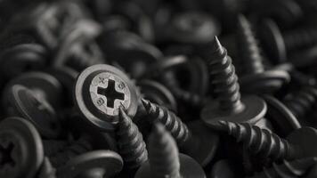 A detailed macro shot of black drywall screws for metal studs with cross-shaped heads arranged in a dense pile. Monochromatic image of drywall screws suitable for industrial or mechanical backgrounds. photo