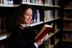 Smiling woman reading a book inside a brightly lit library environment photo