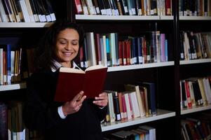 Smiling woman reading a book in a library among bookshelves photo