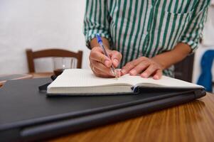 Close-up of a person writing notes in a lined notebook at a table photo