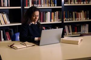 Woman studying in library using laptop with open books on the table photo