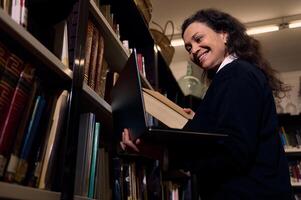 Smiling librarian holding a book inside a library surrounded by shelves of books photo