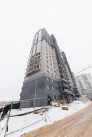 Amidst the Winters Embrace A Towering Residential Structure Rising from a Snow-Covered Landscape, Encircled by the Tools of Progress. photo