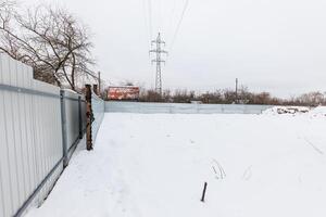 Silent Winter Escape A desolate snowy lot enclosed by metal, under a moody sky, whispers stories of solitude amidst barren trees and wiry power lines. photo