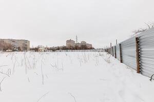 Winters Embrace A Snow-Covered Field Framed by Rusting Fencing and Silent Structures Beyond photo