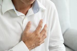 asian man working hard have chest pain caused by heart disease, leak, dilatation, enlarged coronary heart, press on the chest with a painful expression photo