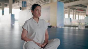 Finding Inner Peace. A woman in white clothing sits in a meditative pose in a spacious, serene indoor environment, radiating tranquility and focus. video
