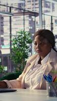 Vertical Stressed black business leader working in discomfort with a headache, feeling overburdened and uncomfortable at the office. Female general director deals with anxiety and fatigue. Camera B. video