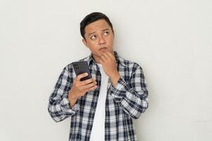 man thinking and concentrating while holding handphone. Asian student thinking and looking for ideas while holding phone photo